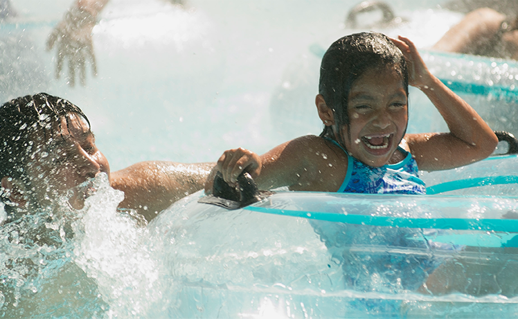 Young girl smiling and floating on inner-tube in pool with Dad